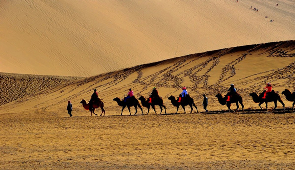 Tourists ride camels on the Mingsha Sand Dunes during a visit to Crescent Moon Spring on the outskirts of Dunhuang county of northwest China's Gansu province. [Photo: China Daily]