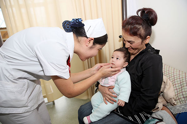 A nurse from the Hospital of Xinjiang Traditional Uyghur Medicine, attends to a mother from Uzbekistan, along with her daughter, who was born in the facility in Urumqi, capital of the Xinjiang Uygur autonomous region.[Photo：Xinhua]