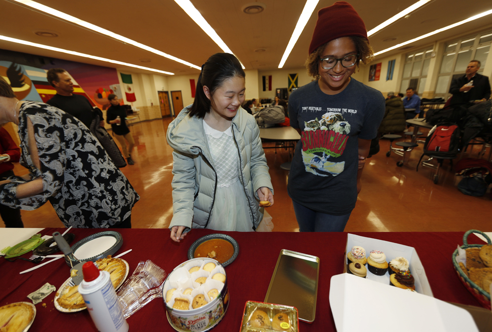 Miaofan Chen, left, works her way through the serving line with Thandi Glick during a potluck meal for Chinese exchange students and their host families at a school in Denver, Jan. 27, 2017. [Photo: AP]