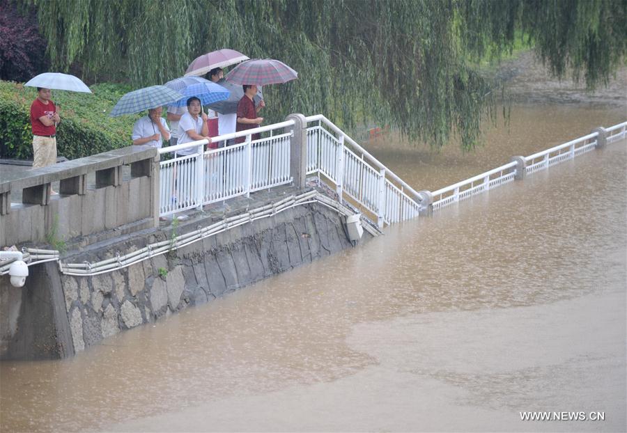 People stand on the flooded bank at Changsha, capital of central China's Hunan Province, July 1, 2017. At 11 a.m. Saturday, the water level of Xiangjiang River, a major river in the province, rose up to 38.37 meters at Changsha hydrological station, 2.37 meters above the alarm level. [Photo: Xinhua]
