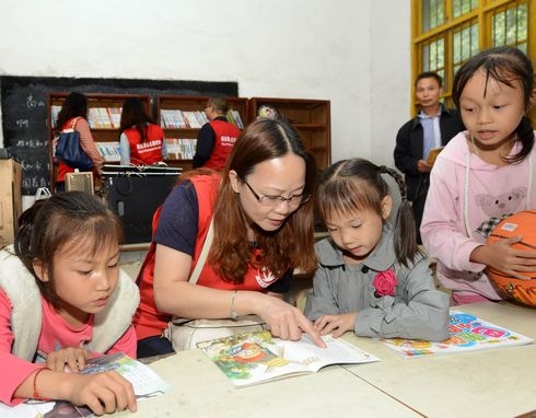 A volunteer reads a story book with left-behind children. [File photo: jxnews.com.cn]